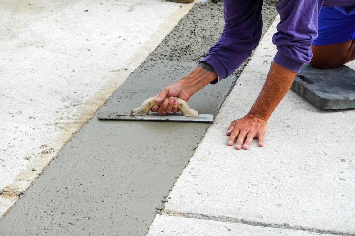 Person using a trowel to smooth wet concrete in a narrow groove on a concrete surface.