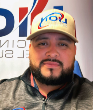 Man with a beard wearing a baseball cap and jacket in front of a logo.