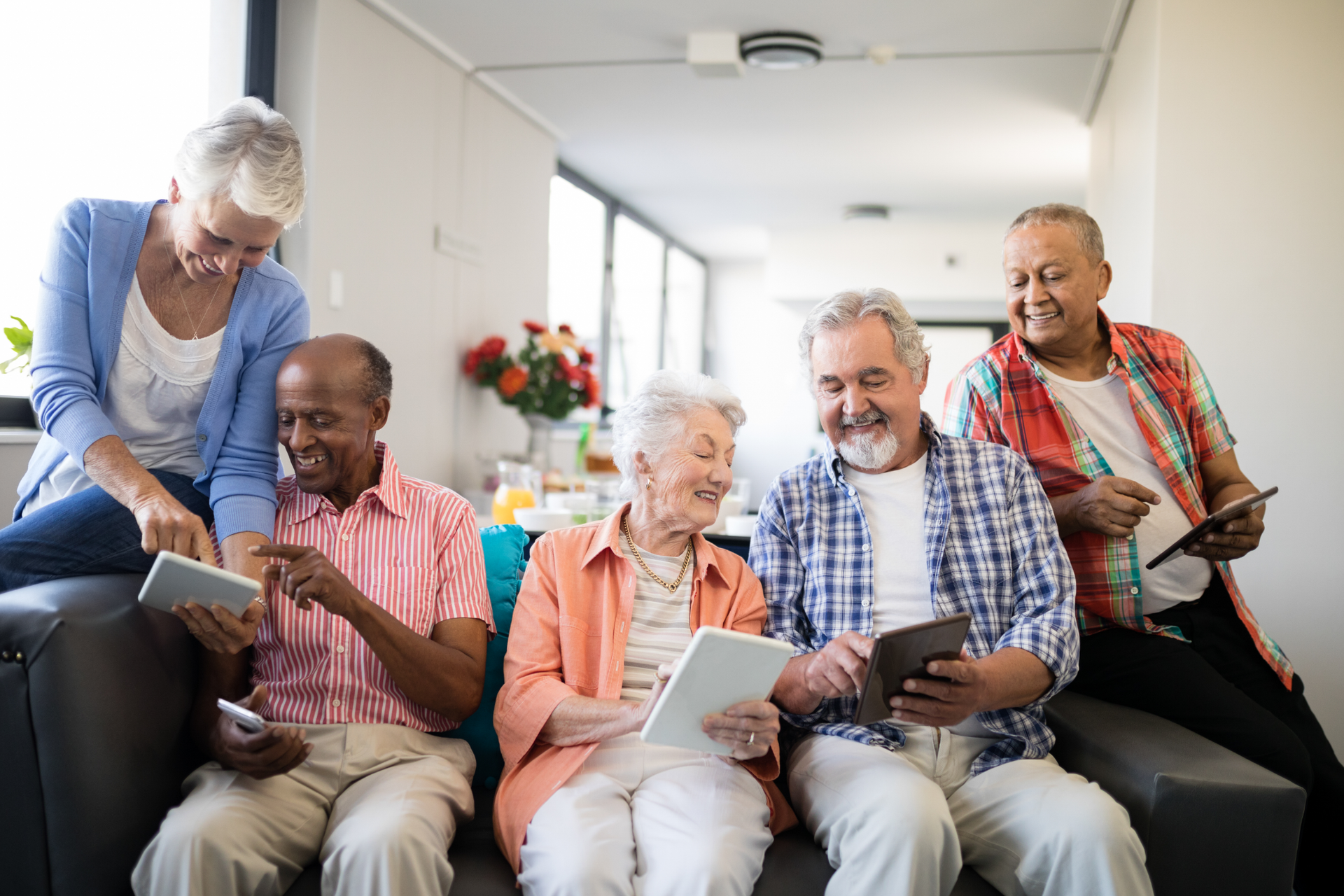 Group of people using tablets on a couch indoors. Smiling, looking at screens.