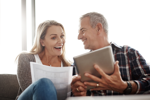 Smiling couple looking at papers and tablet, sitting on a couch.