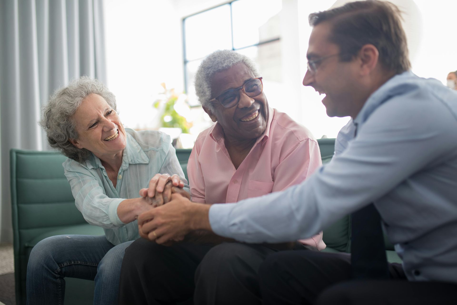 Three people smiling and interacting indoors. Older couple sits with a younger man.