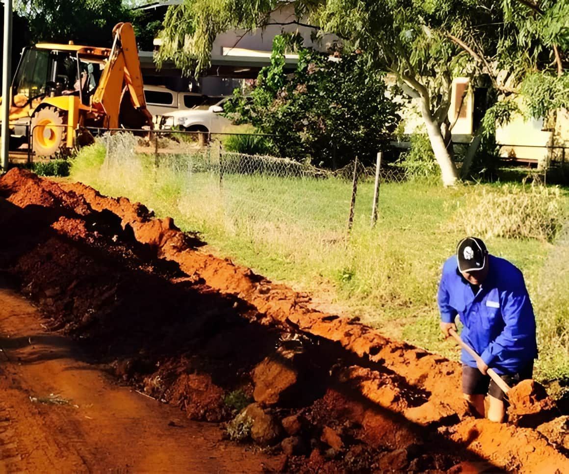 Man Digging Trench Next to A Road with Backhoe — SDA Plumbing in Alice Springs, NT