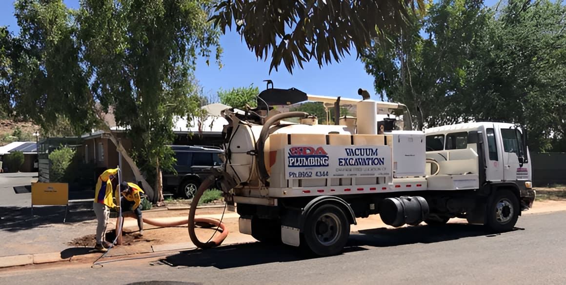 A worker operating a white vacuum truck on a street, sucking material from the ground near trees and houses. — SDA Plumbing in Alice Springs, NT