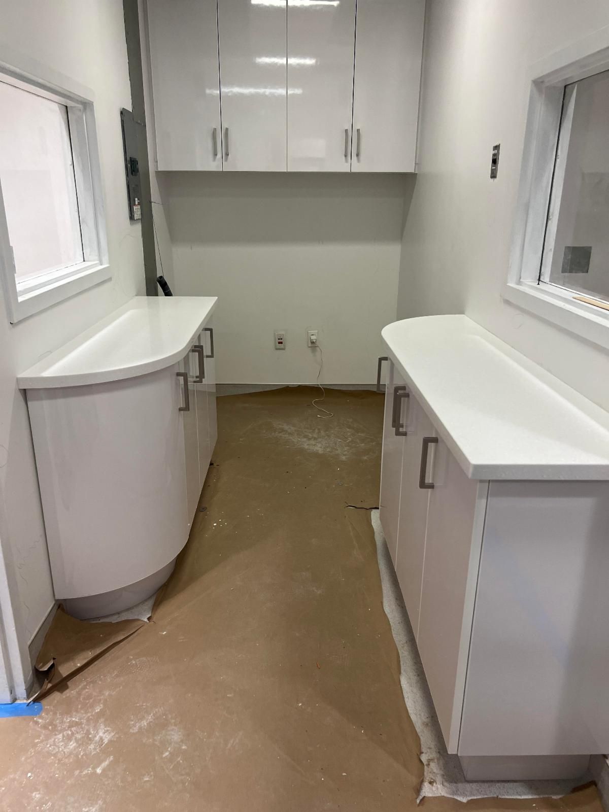 White cabinetry in a small room, two countertops with cabinets, and overhead cabinets. Beige flooring.