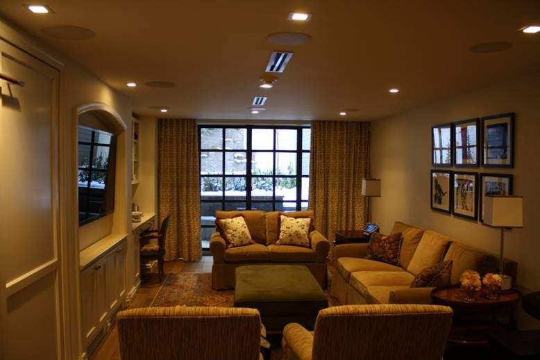 Cozy living room with neutral tones, two sofas, chairs, large window with curtains, and recessed lighting.