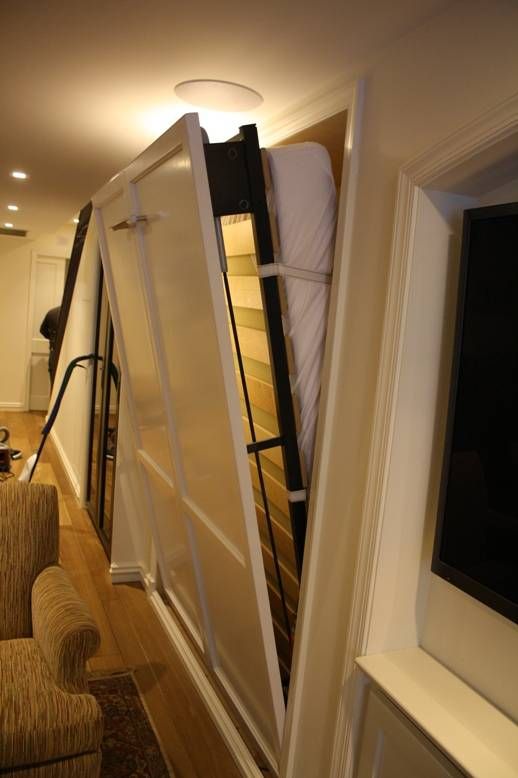 A white Murphy bed partially lowered from a wall, revealing a mattress. Interior room.