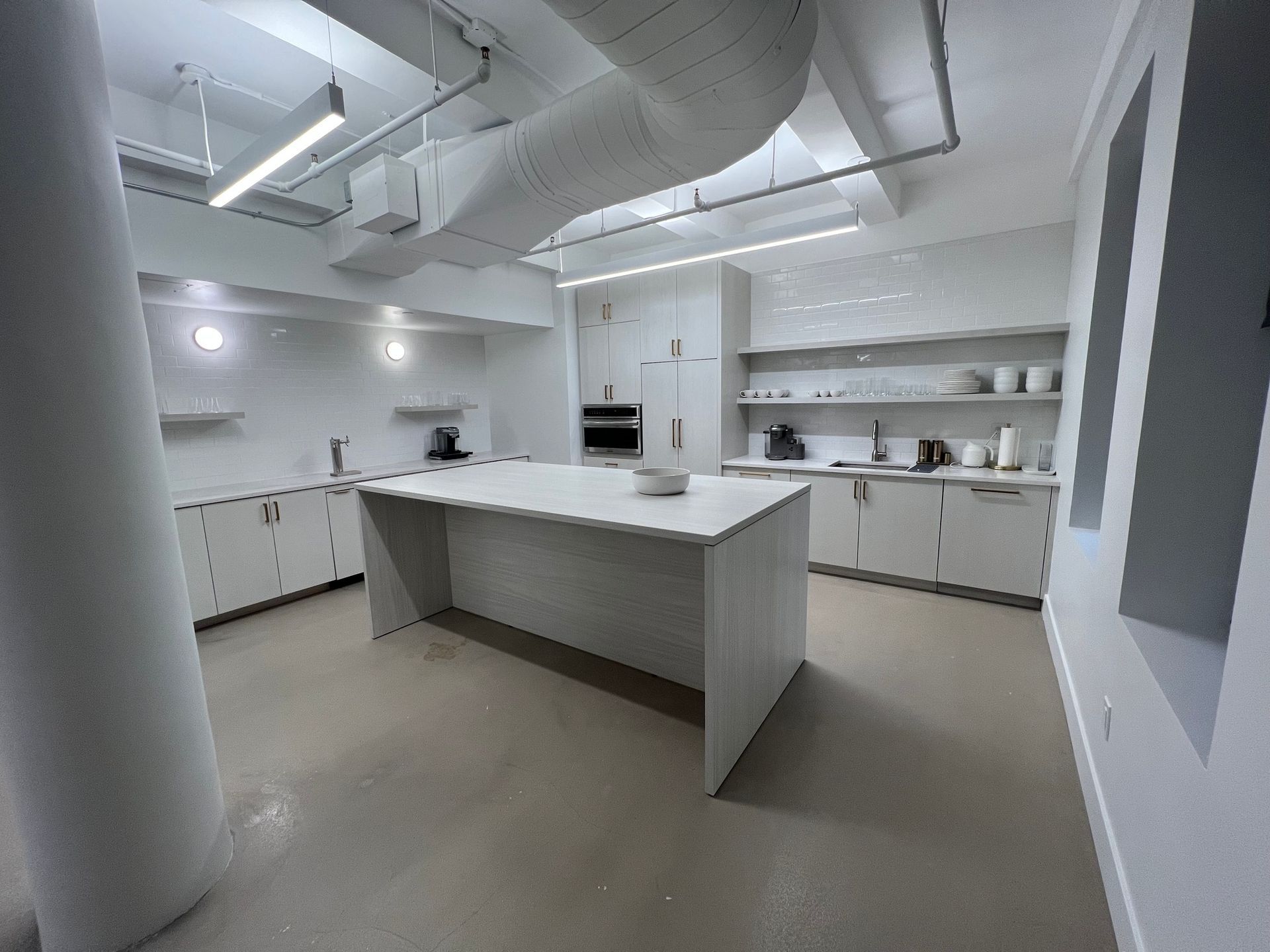 Modern white kitchen with island, cabinets, appliances, and a large support column.