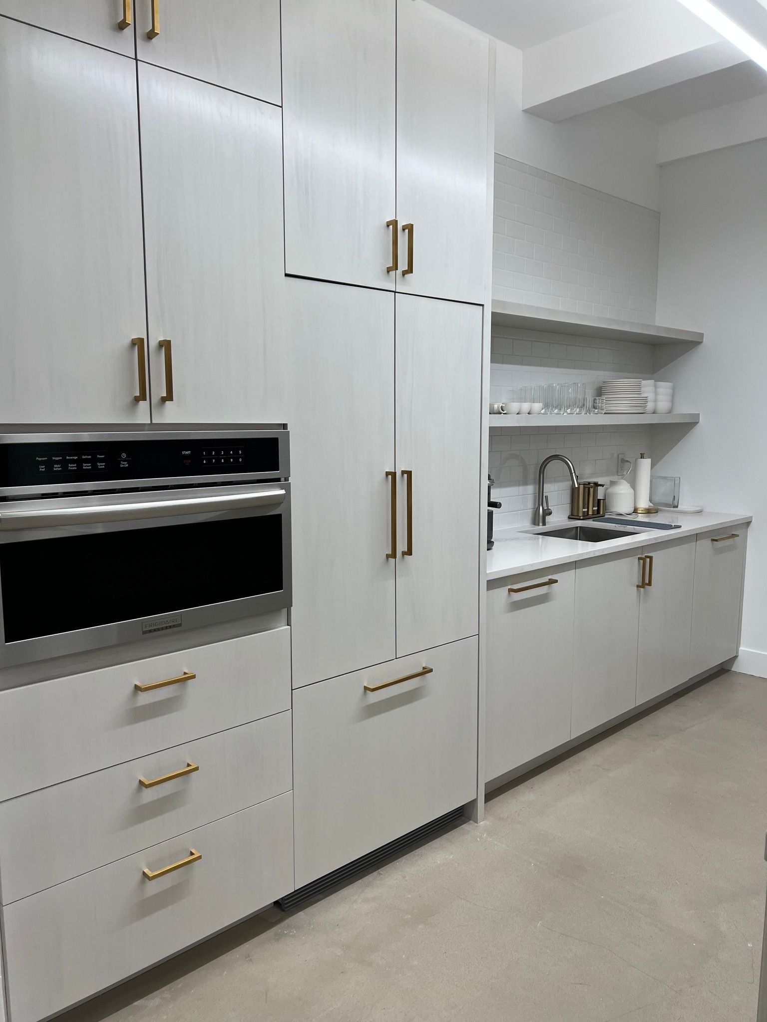 A modern kitchen with light gray cabinets, gold hardware, and stainless steel appliances.