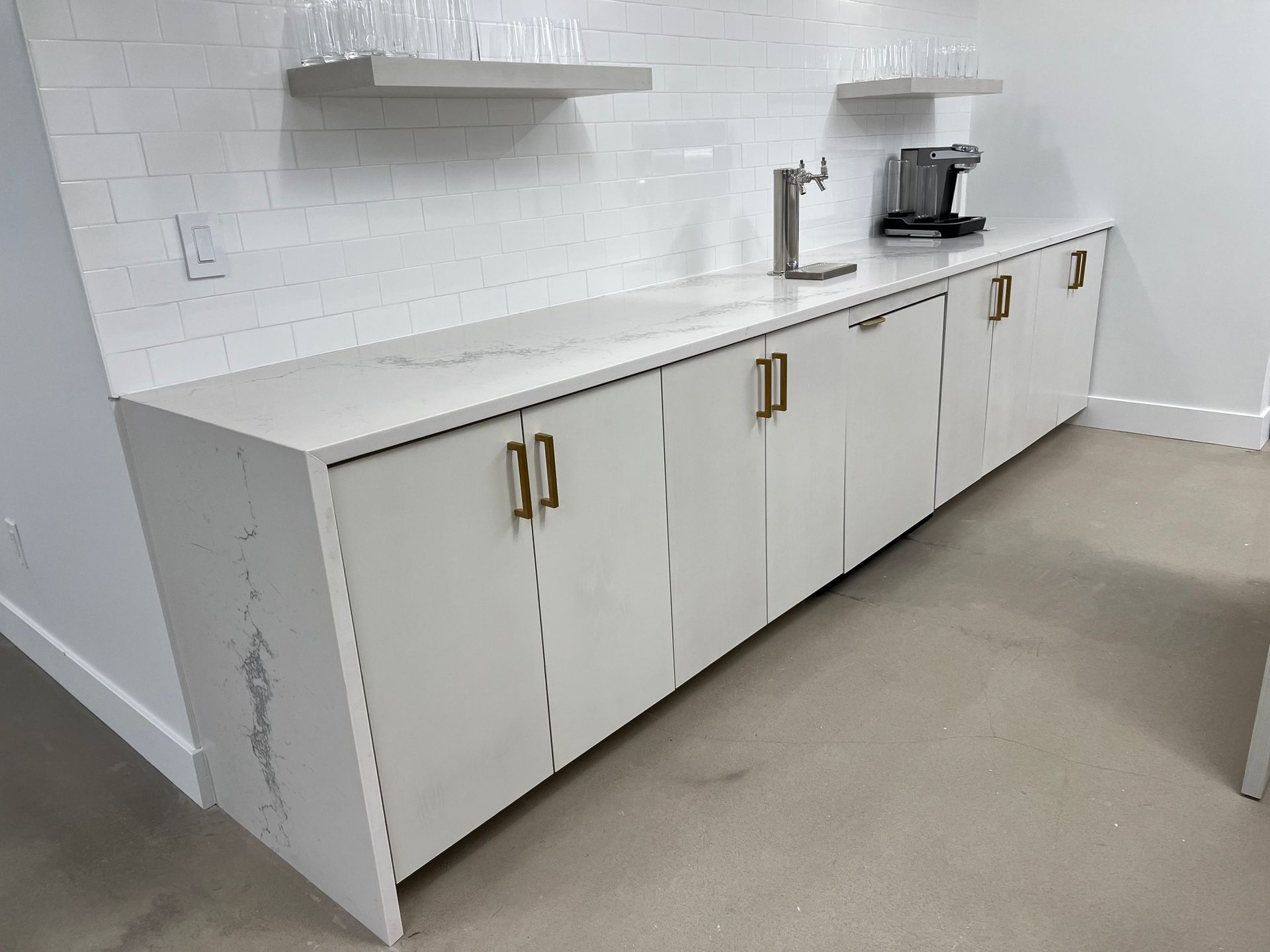 White cabinet with gold handles and marble countertop in a white-tiled kitchen area.