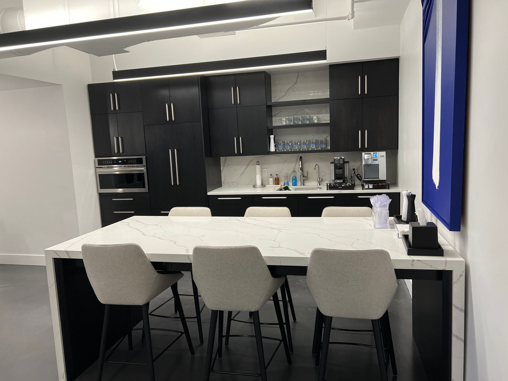 Modern office kitchen with black cabinets, white countertop, and bar seating.