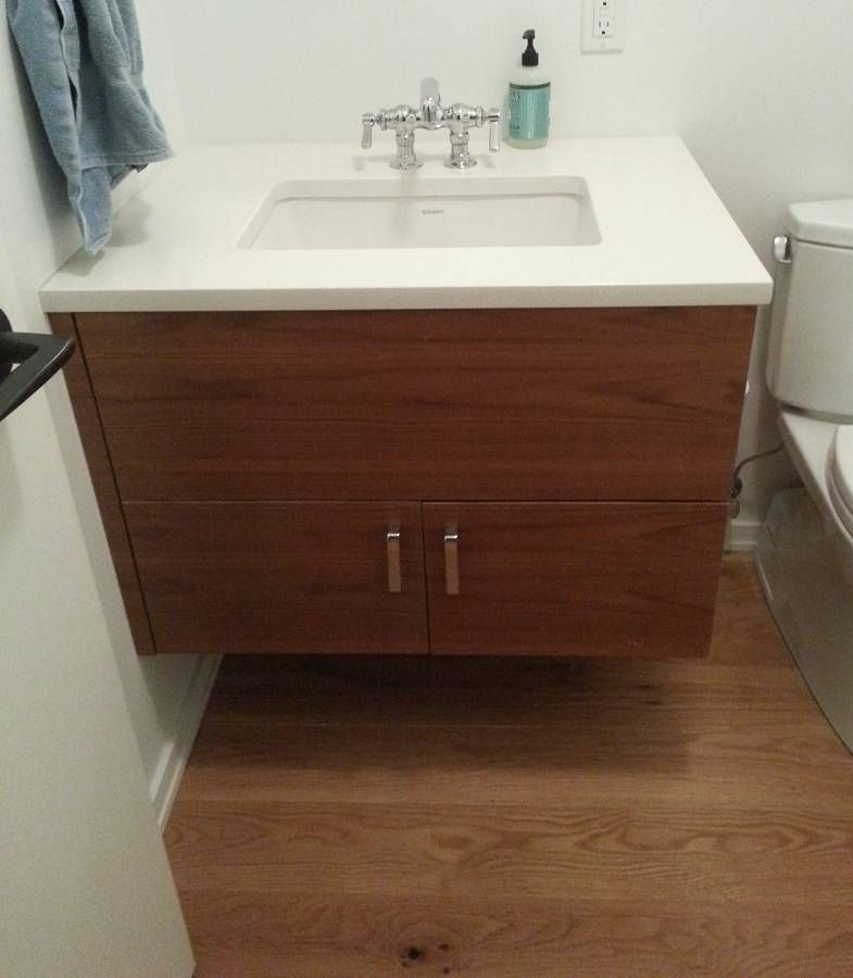 Wooden bathroom vanity with a white countertop and sink, mounted on a wood floor.
