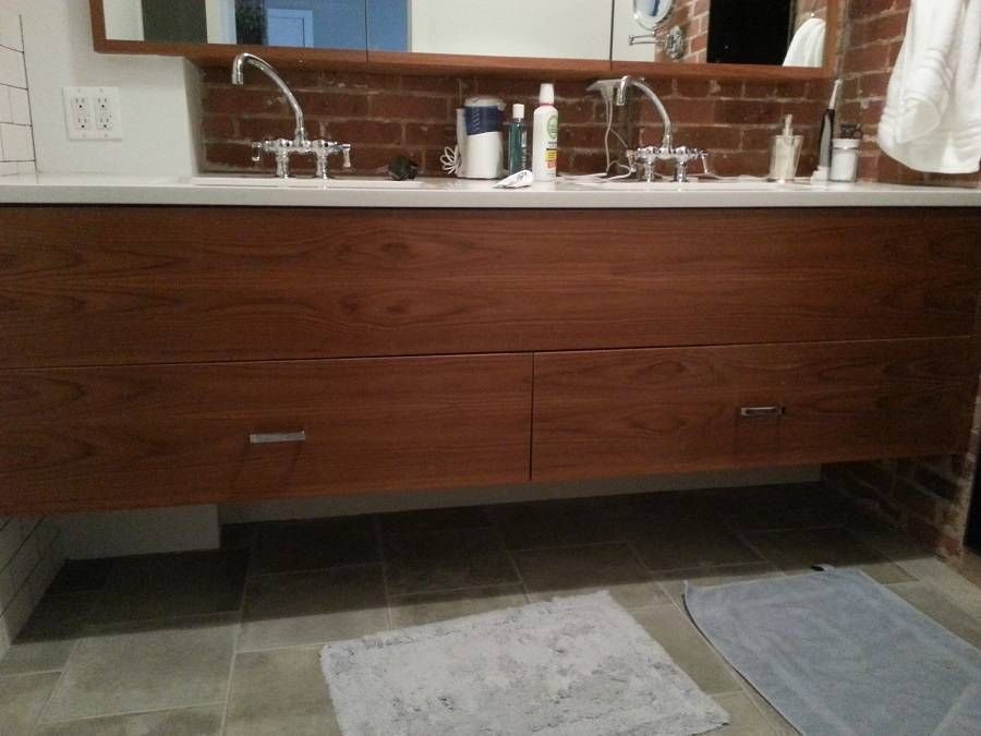 Floating wood bathroom vanity with two sinks and drawers, brick backsplash.