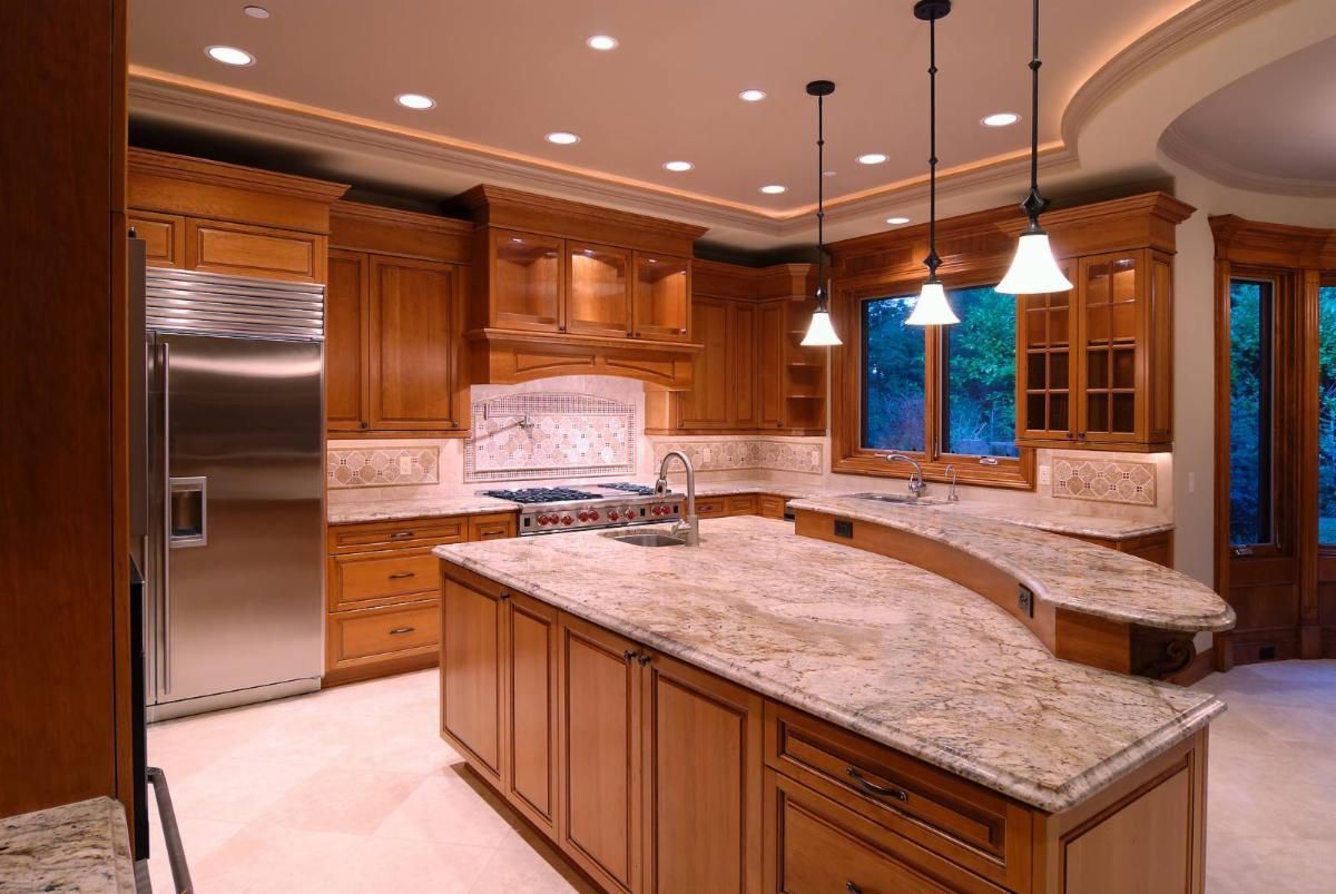 Kitchen with wood cabinets, granite countertops, stainless steel refrigerator, and pendant lights.
