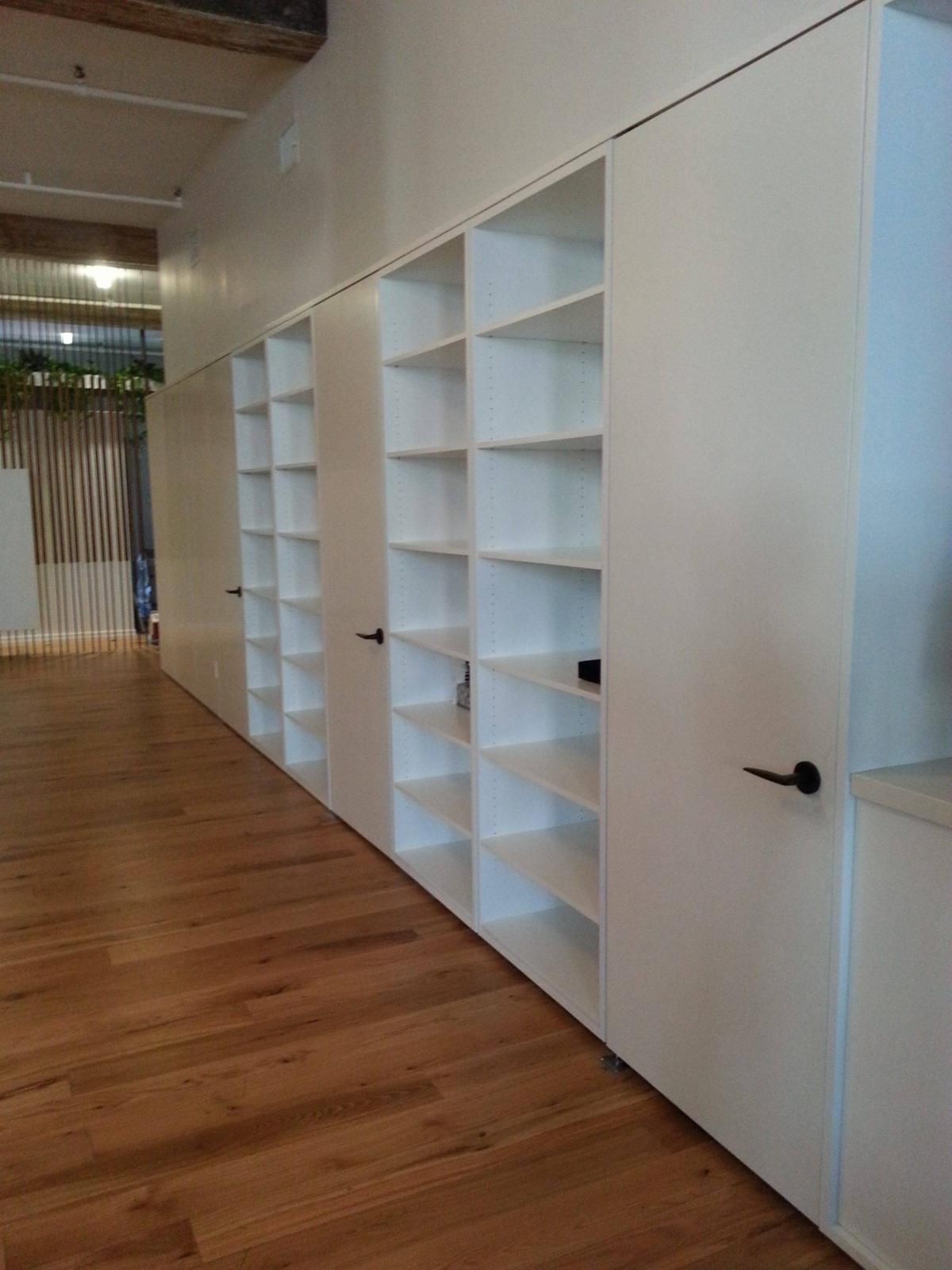 White built-in shelving unit with closed doors and open shelves against a long wall with wooden flooring.