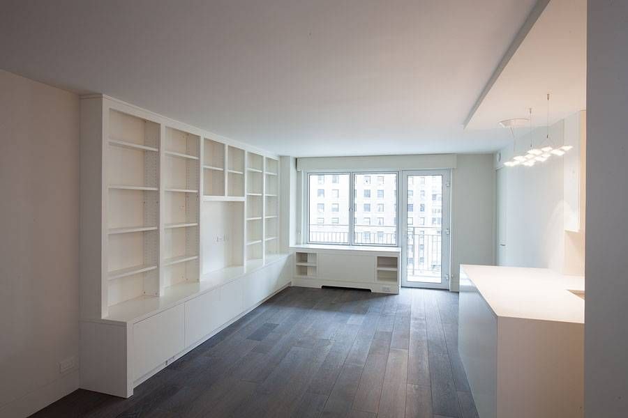 Modern living room with built-in white shelving, dark wood floor, and a balcony.