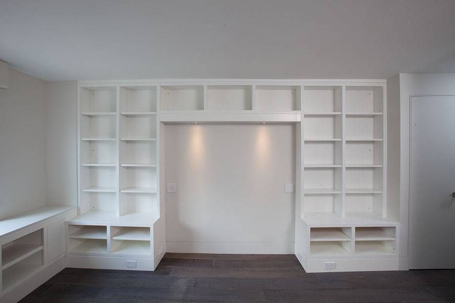 White built-in bookshelves on either side of a recessed wall, with dark flooring.