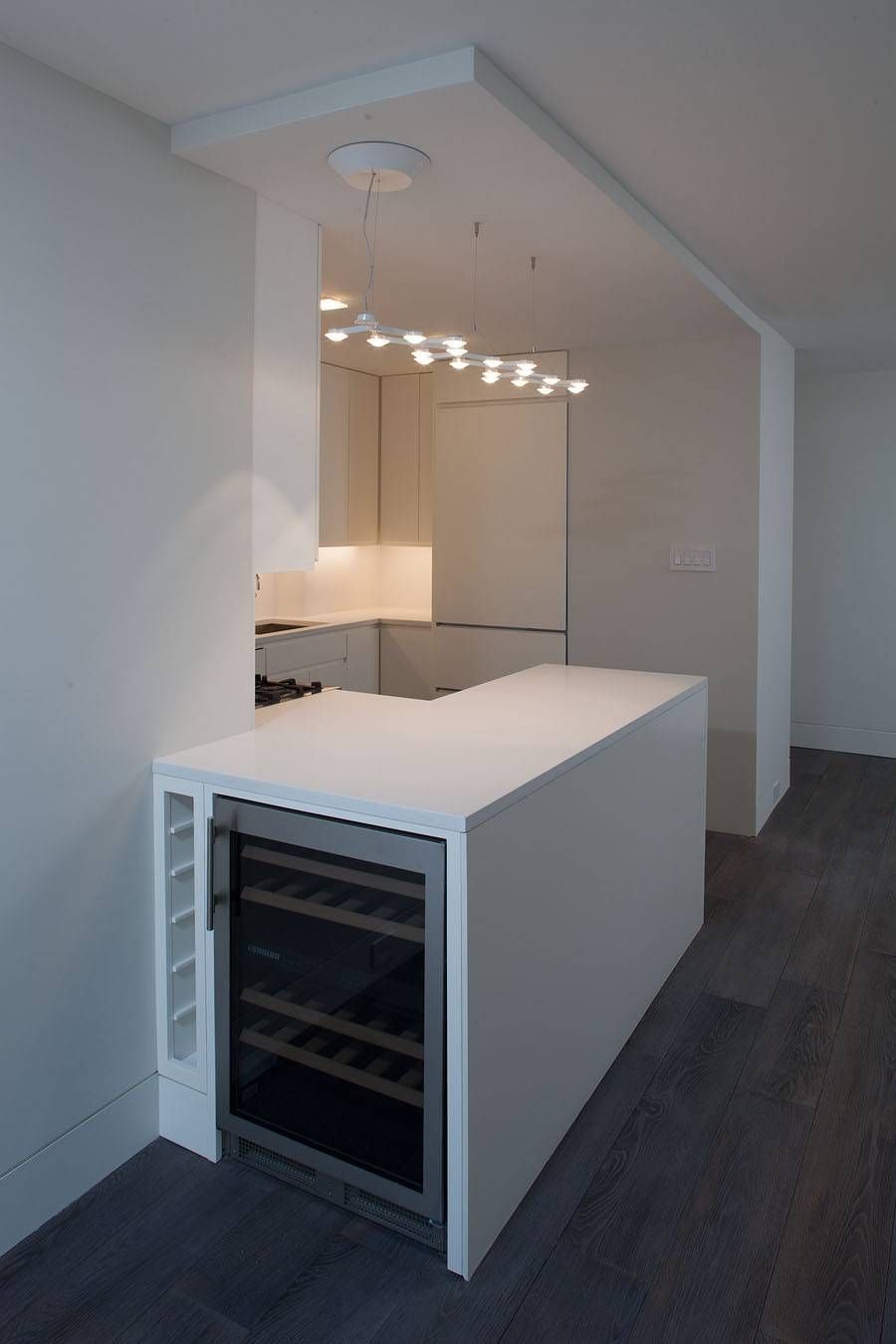 Modern kitchen with white island and wine fridge; pendant lights hang above the stove.