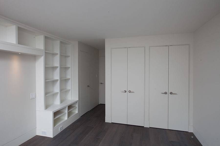 Empty room with white built-in shelves and closet doors; dark wood floor; white walls and ceiling.