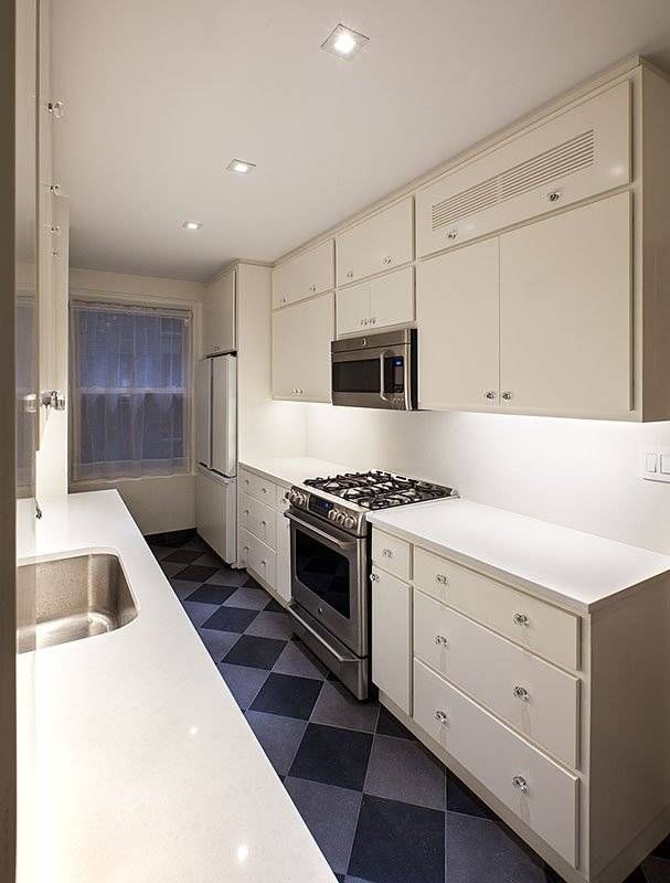 Narrow, white kitchen with stainless steel appliances, white countertops, and checkered floor.