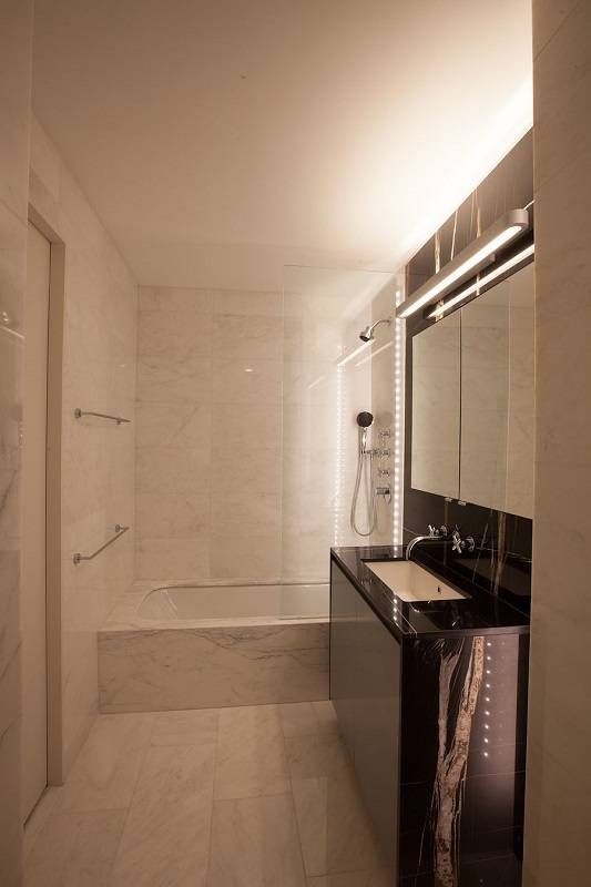 Modern bathroom with marble walls and black vanity, a glass shower, and a single sink.