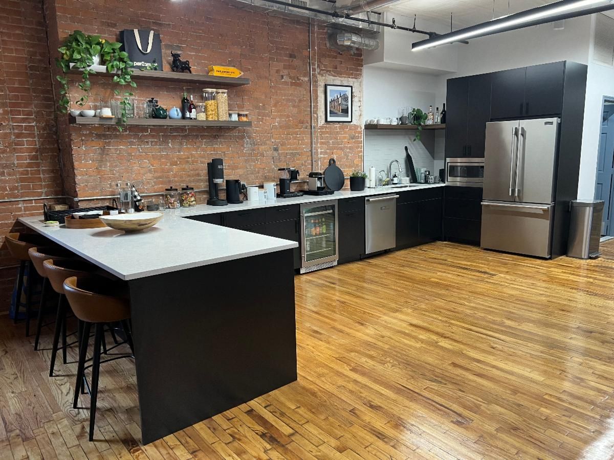 Modern kitchen with exposed brick walls, dark cabinets, and a large island with bar stools.
