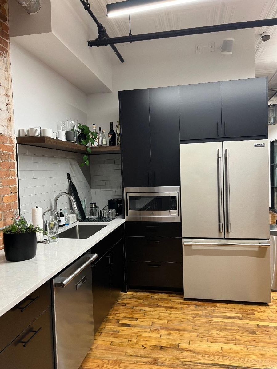 Modern kitchen with black cabinets, stainless steel appliances, and wooden floors.