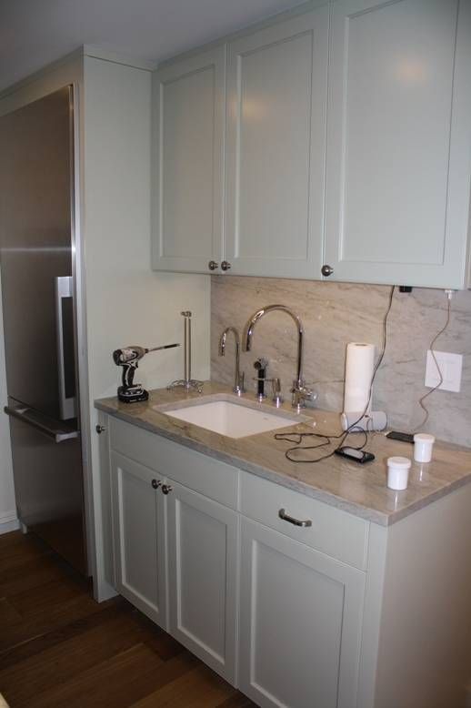 Light green cabinets with a white sink and stainless steel faucet, in a kitchen.