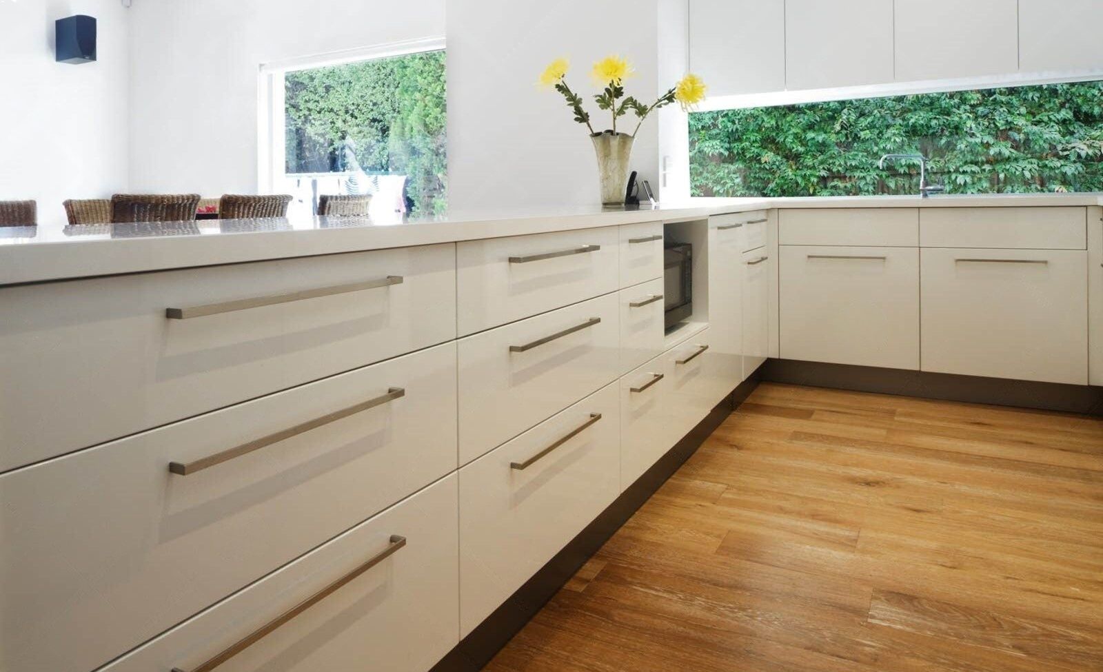 Modern white kitchen with wooden floors and long, horizontal silver handles.