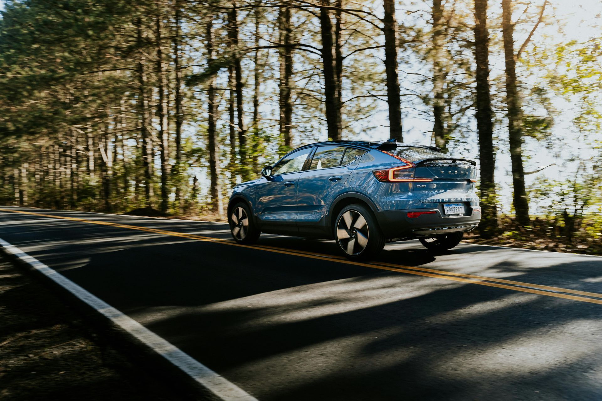 A blue car is driving down a road in the woods.