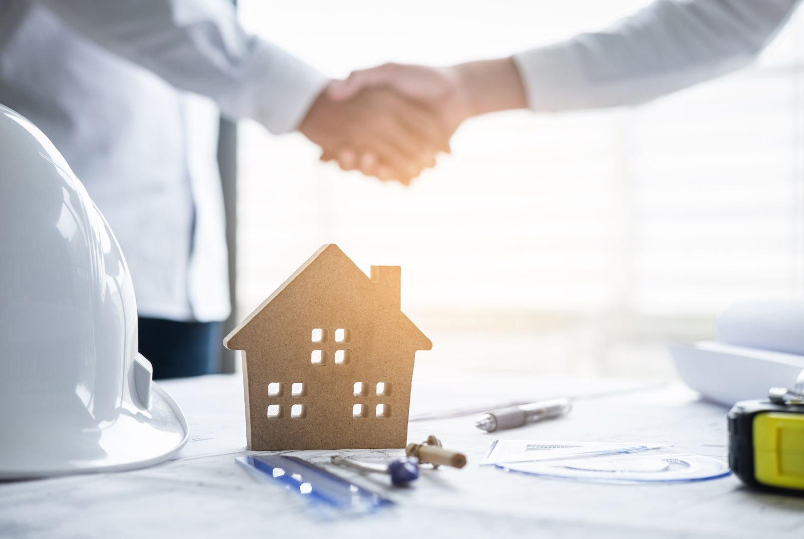 A man and a woman are shaking hands in front of a model house.