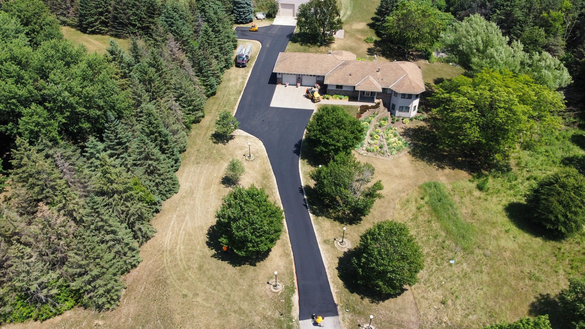 An aerial view of a house and a driveway surrounded by trees.