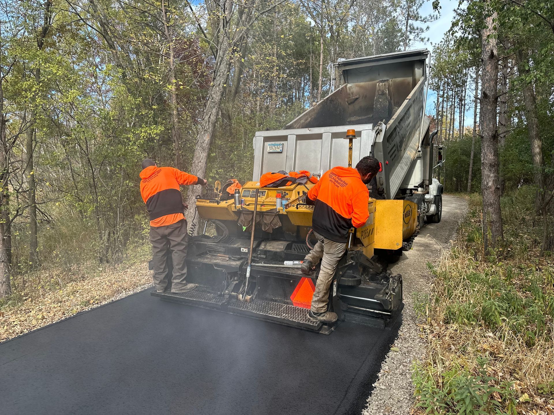 Two men are working on a road next to a dump truck.