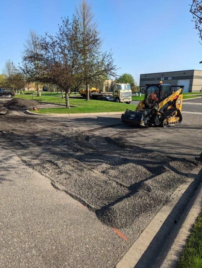 A bulldozer is laying asphalt in a parking lot.