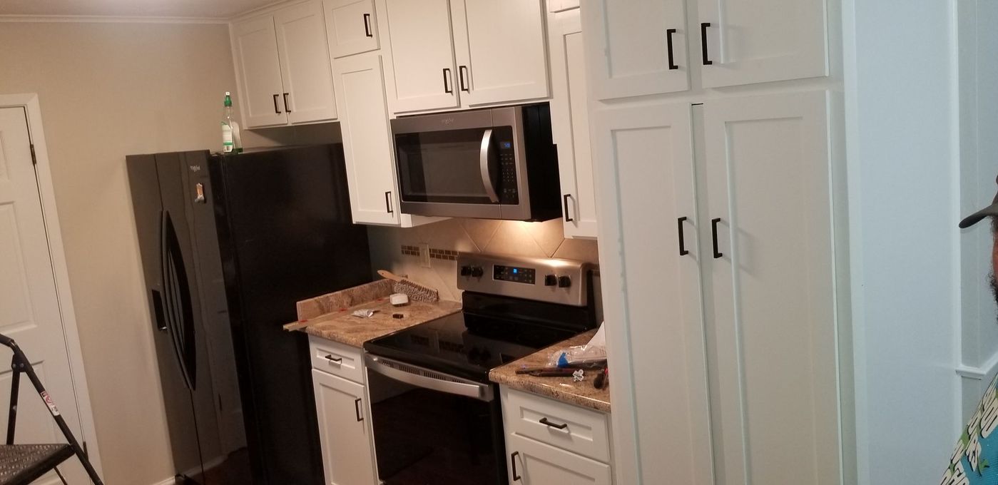 A kitchen with white cabinets , a black refrigerator , a stove , and a microwave.