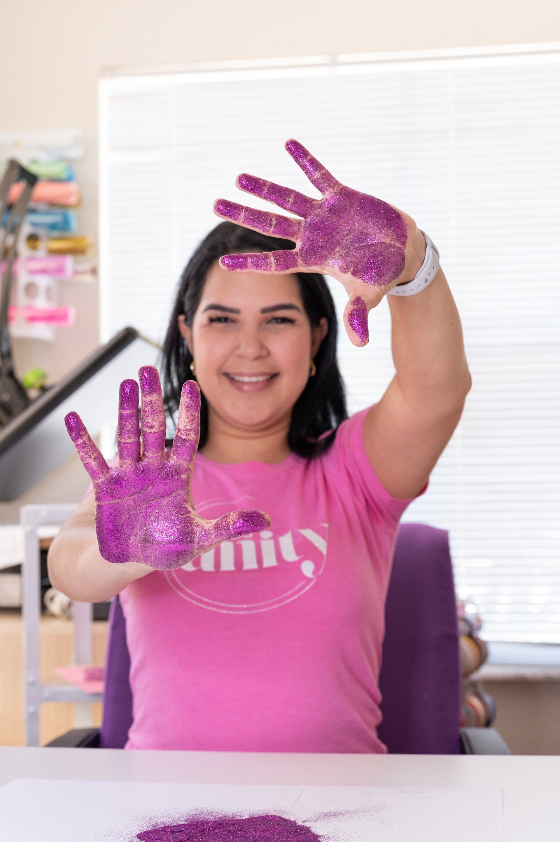 Una mujer con una camisa rosa está sentada en un escritorio con las manos pintadas de púrpura.