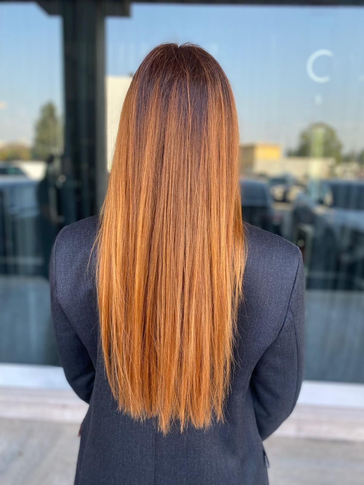 Una persona vista di spalle, con lunghi capelli lisci color rame caldo, che indossa un cappotto scuro, davanti a una vetrina.