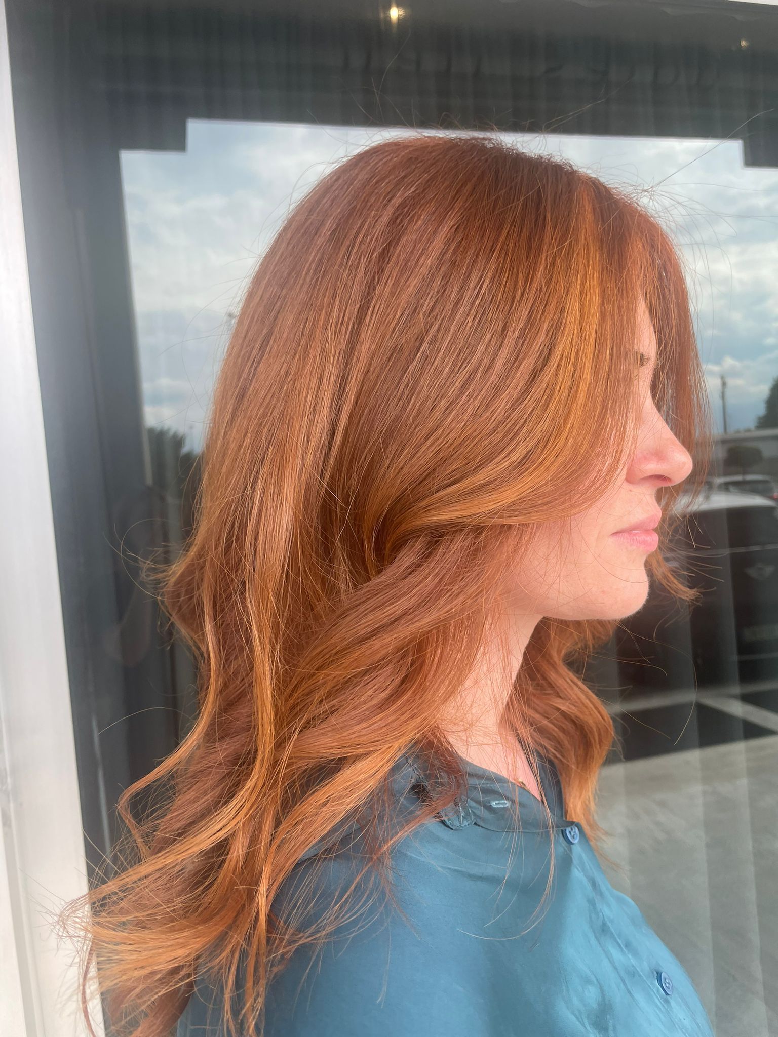 Profilo laterale di una persona con capelli color rame, lunghi fino alle spalle e dalla texture morbida, acconciati in onde delicate.