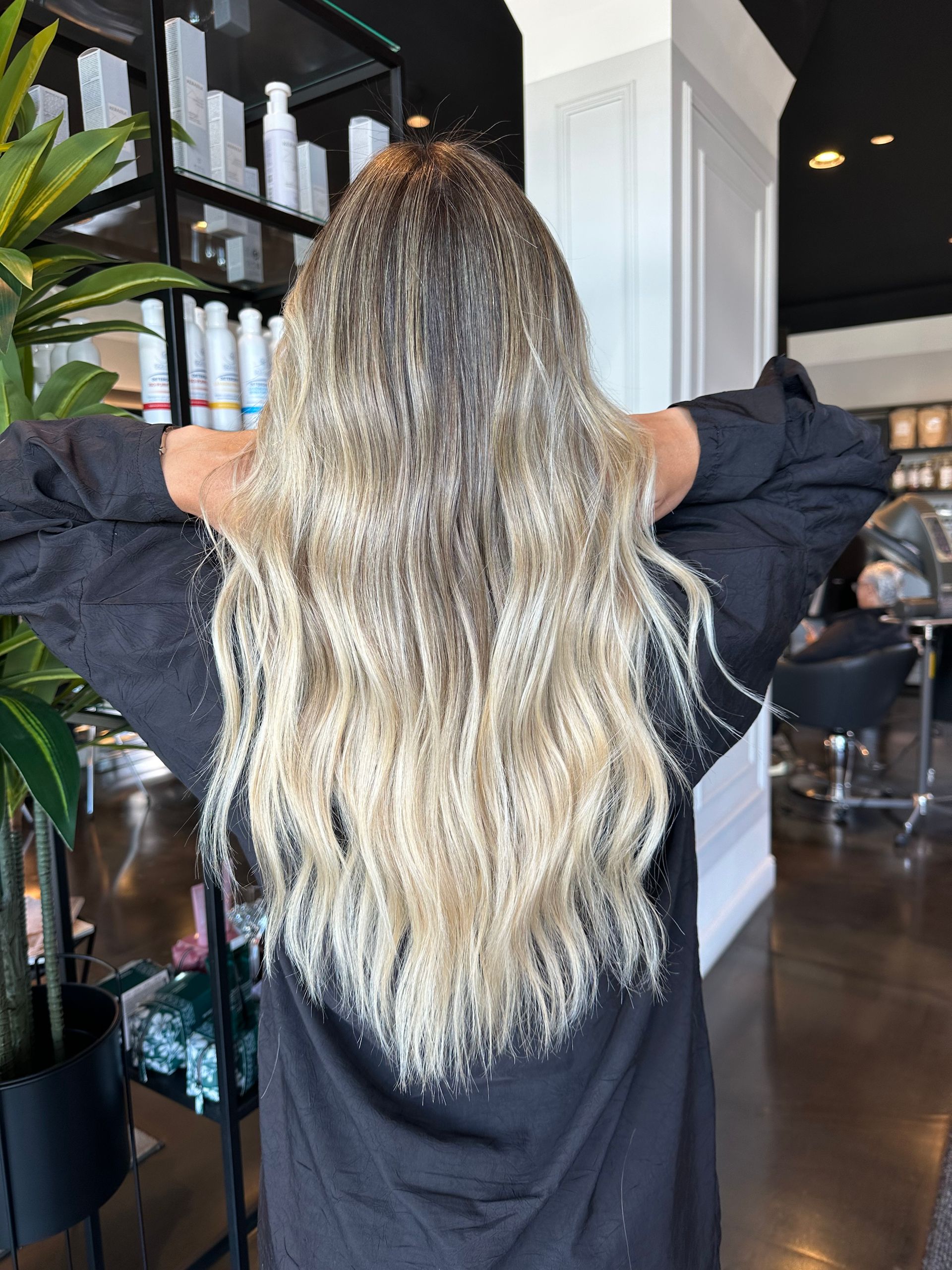 Una persona con lunghi capelli biondi ondulati con tecnica balayage, vista di spalle in un salone di parrucchiere.