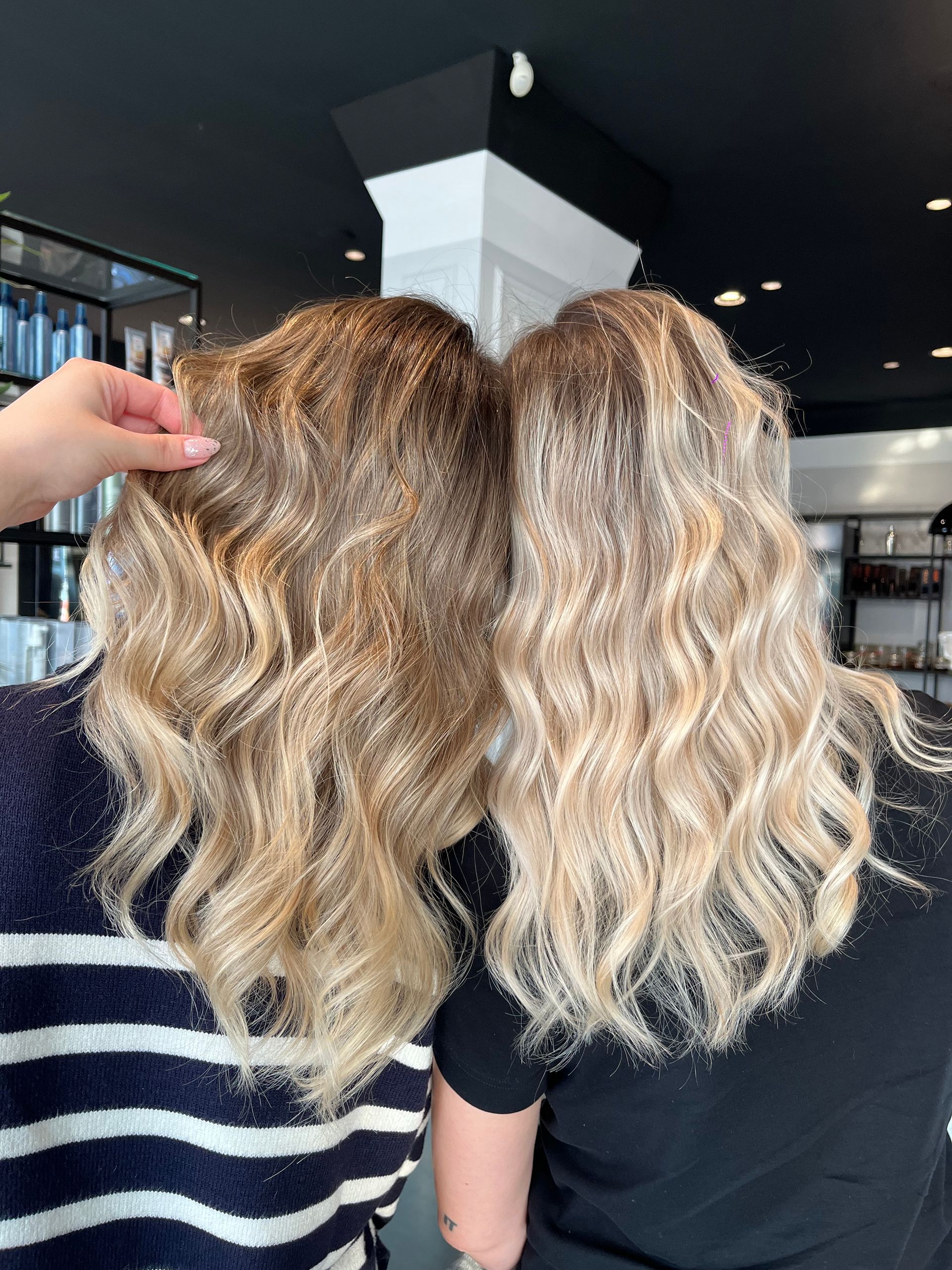 Vista posteriore di due persone in piedi una accanto all'altra in un salone, che mostrano i loro lunghi capelli biondi, ondulati e con mèches.