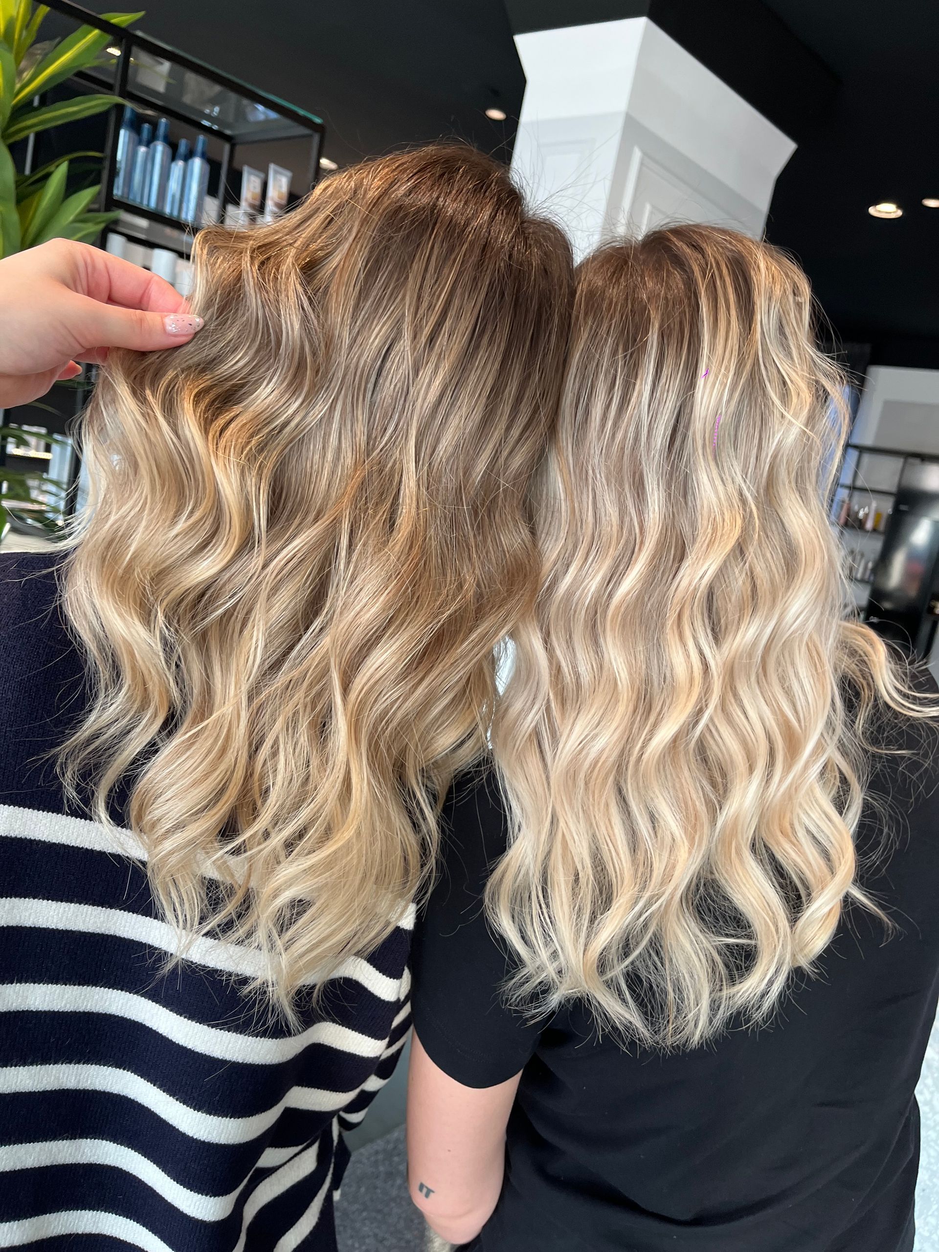 Due persone con lunghi capelli biondi, mossi e con mèches, in piedi una accanto all'altra in un salone di bellezza.