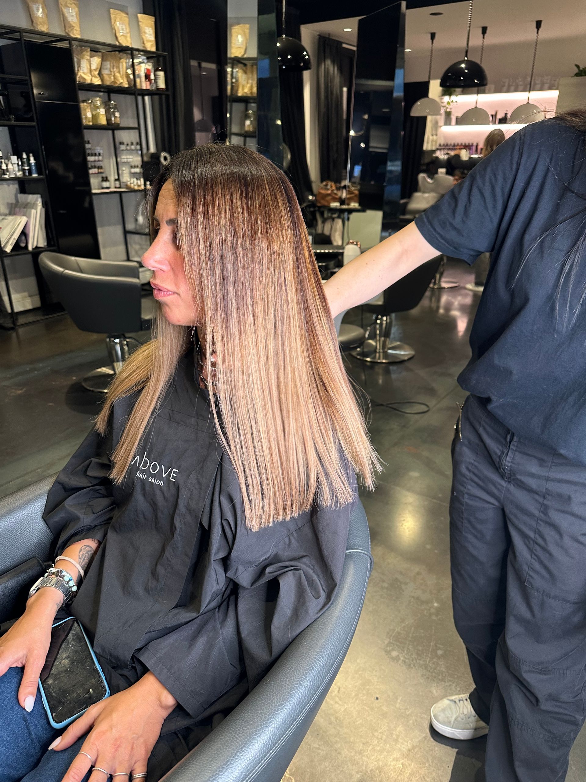In un salone di parrucchiere, un parrucchiere lavora sui lunghi capelli castano chiaro e ondulati di una cliente.