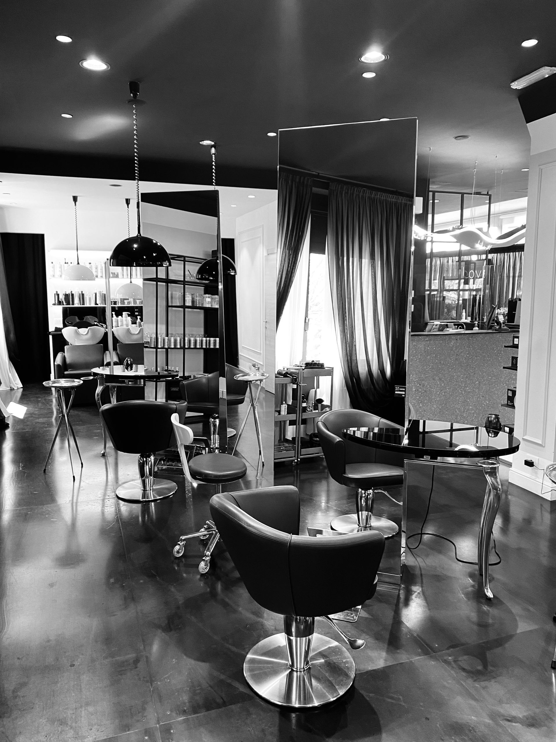 Interno di un moderno salone da parrucchiere monocromatico, con diverse poltrone per lo styling, specchi e lampade a sospensione.