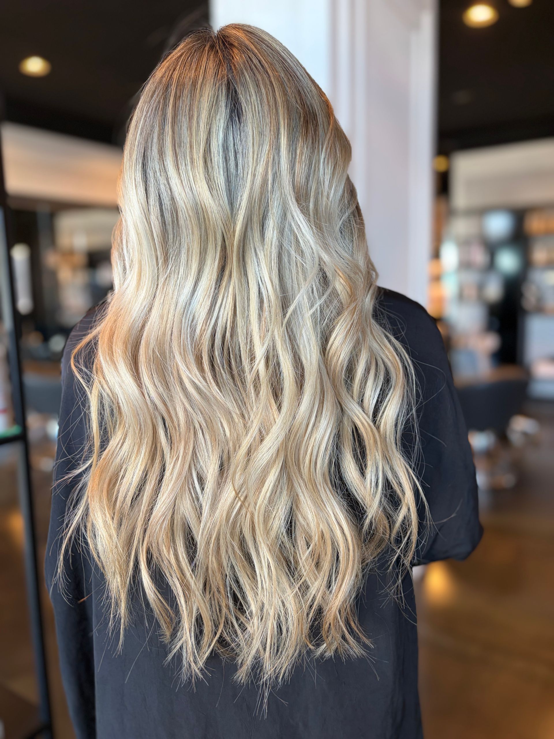 Vista posteriore di lunghi capelli mossi, con mèches castane e bionde, in un salone di bellezza.