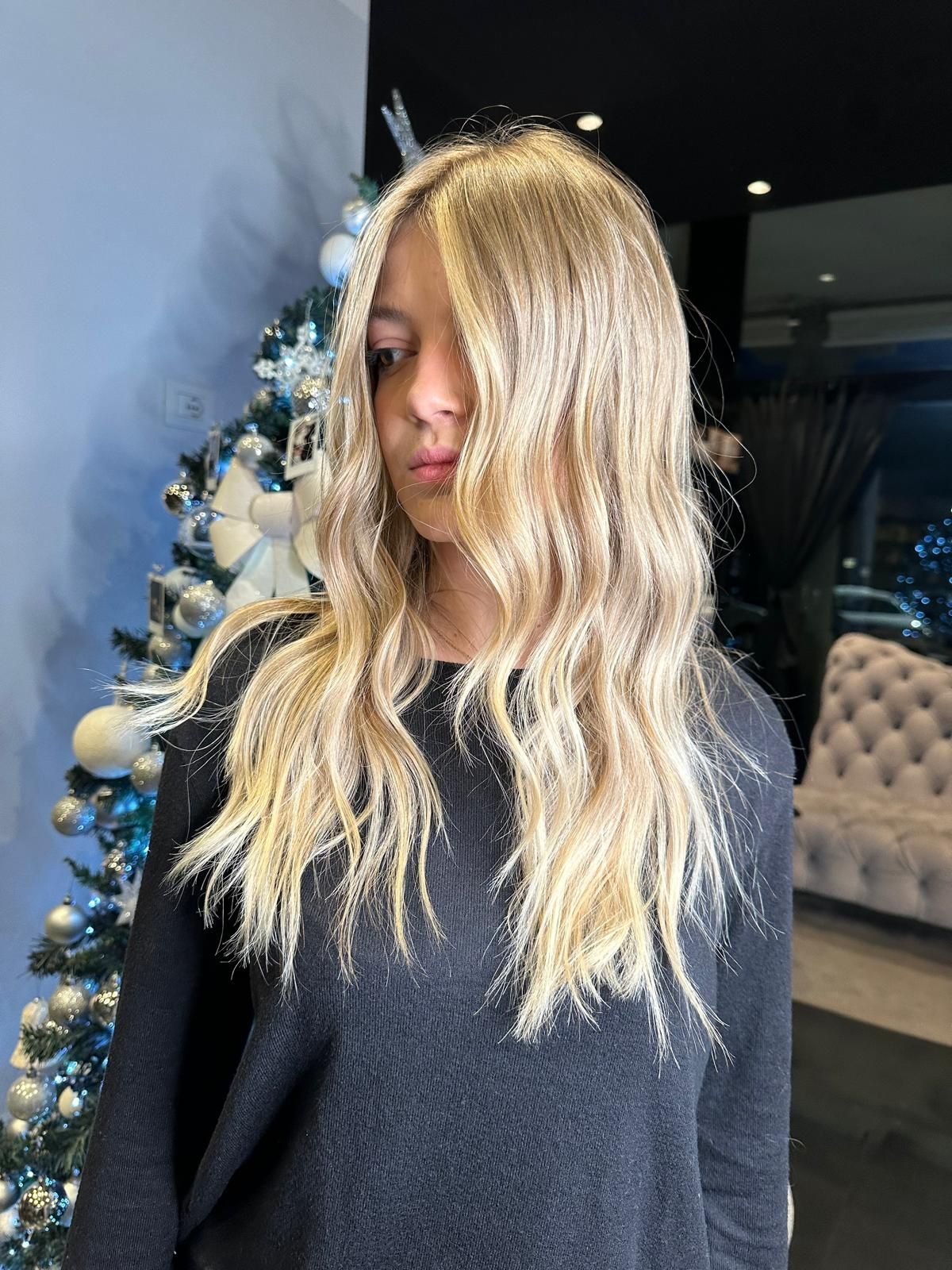 Una persona con lunghi capelli biondi e ondulati è in piedi in una stanza decorata con un albero di Natale.