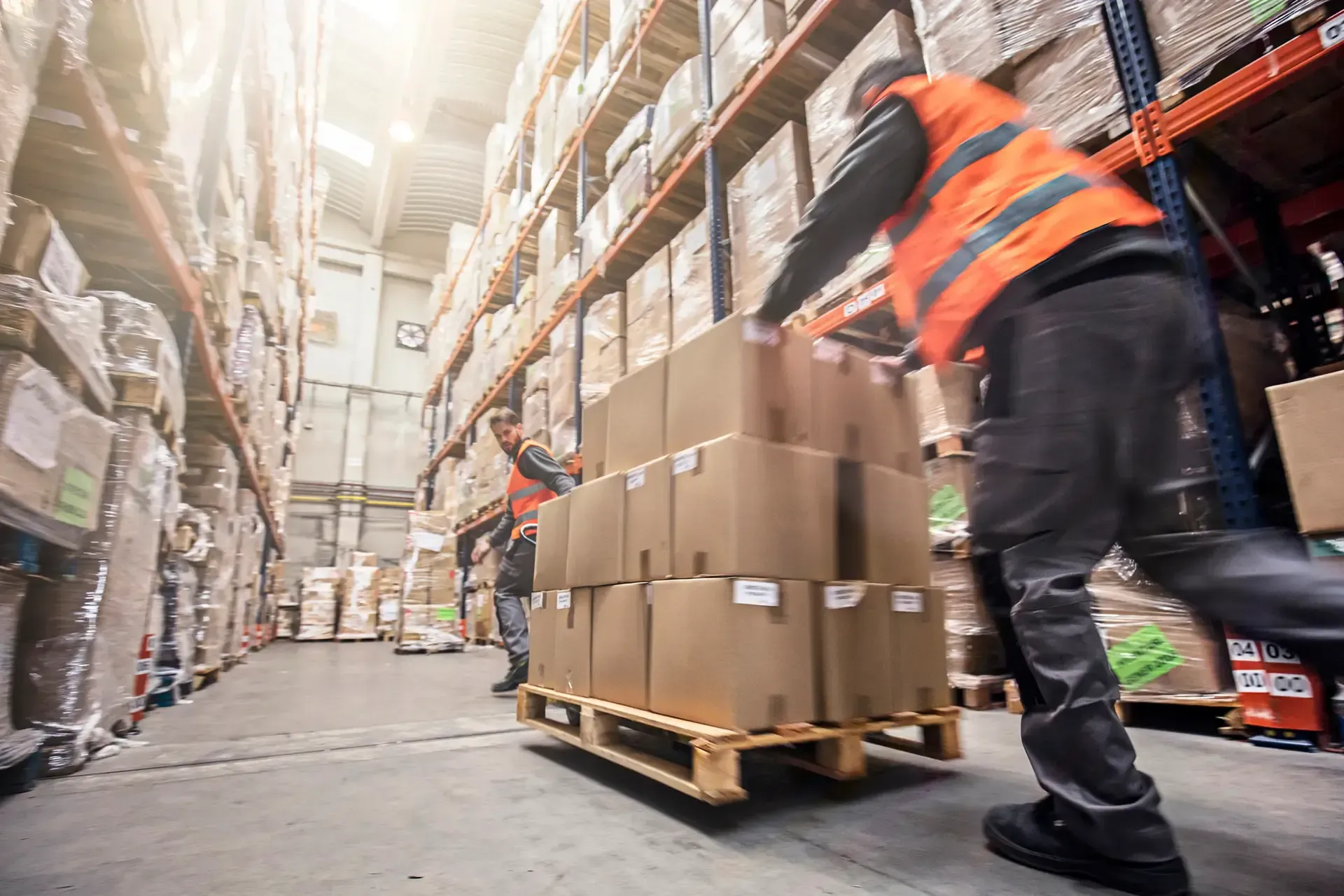 A man is pushing a pallet of boxes in a warehouse.