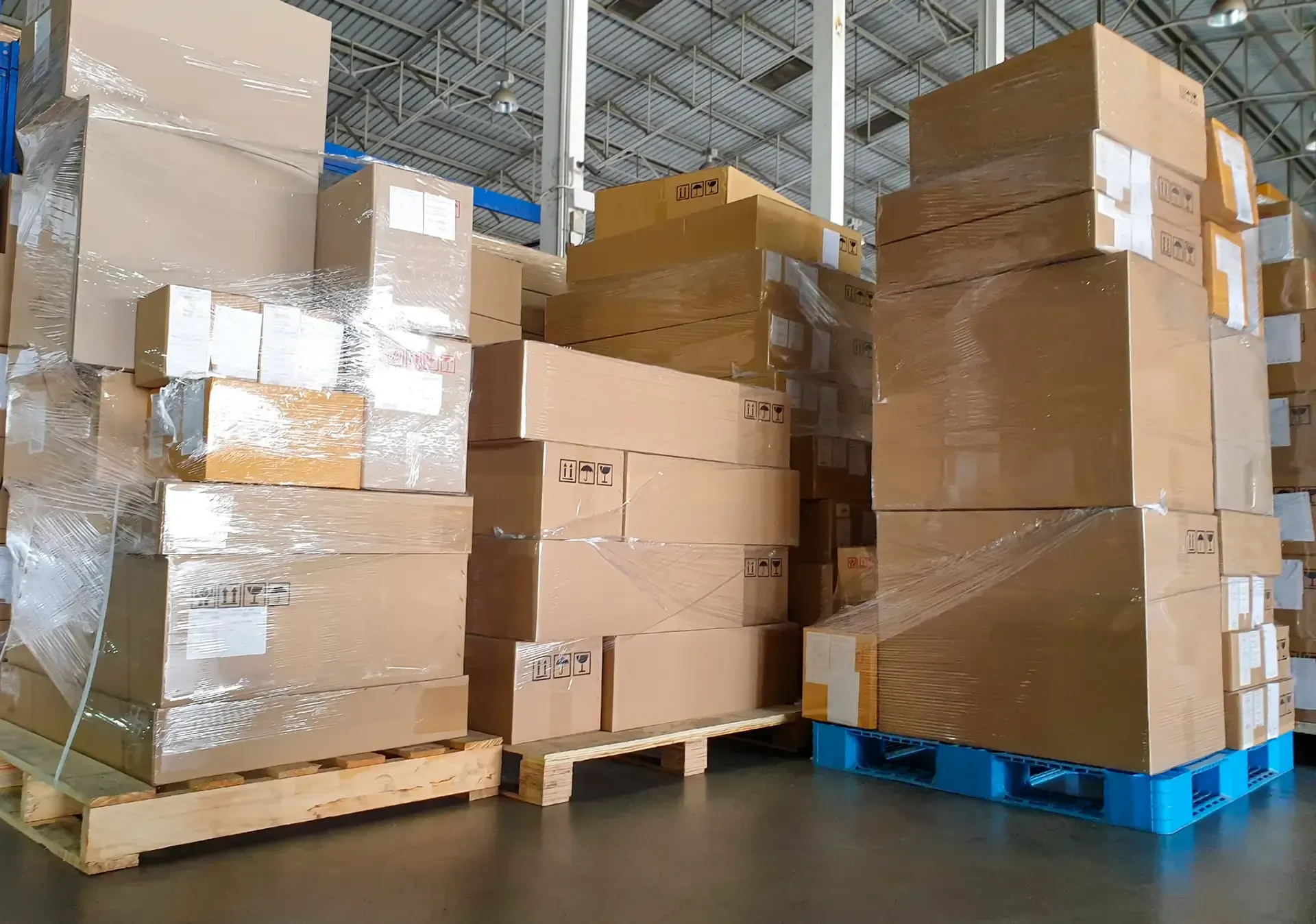 A warehouse filled with lots of cardboard boxes on wooden pallets.