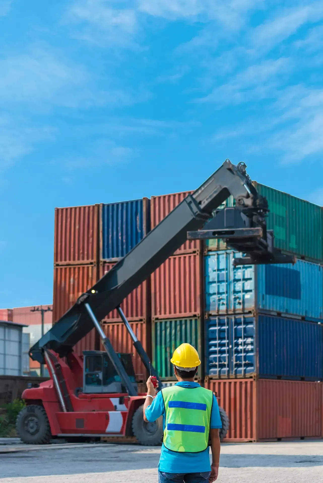 A man in a yellow hard hat is standing in front of a stack of shipping containers.