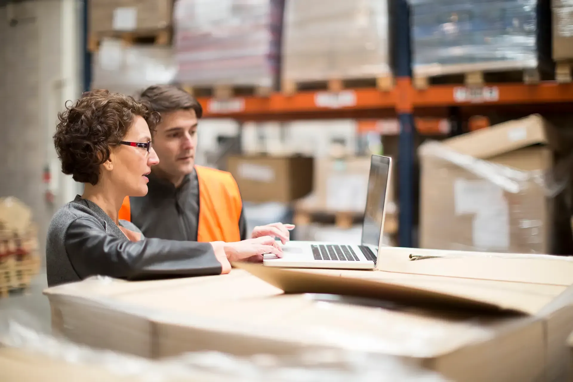 A man and a woman are looking at a laptop in a warehouse.