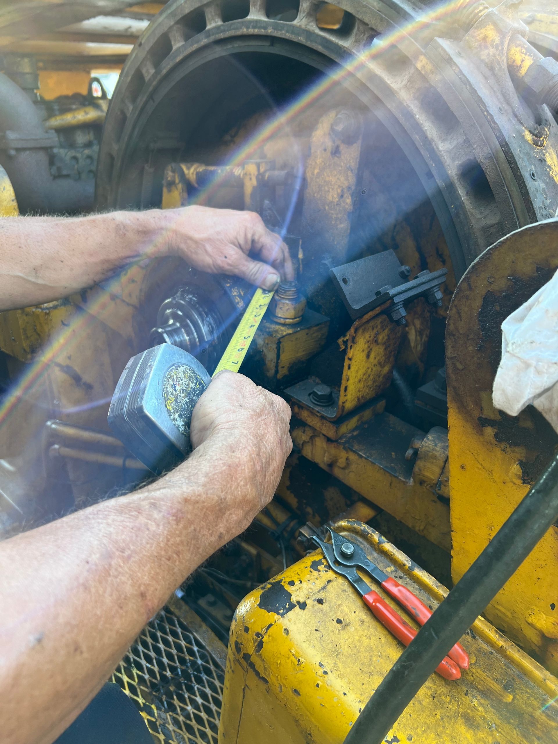 Person measuring machinery with a tape measure. Yellow equipment, tools visible.