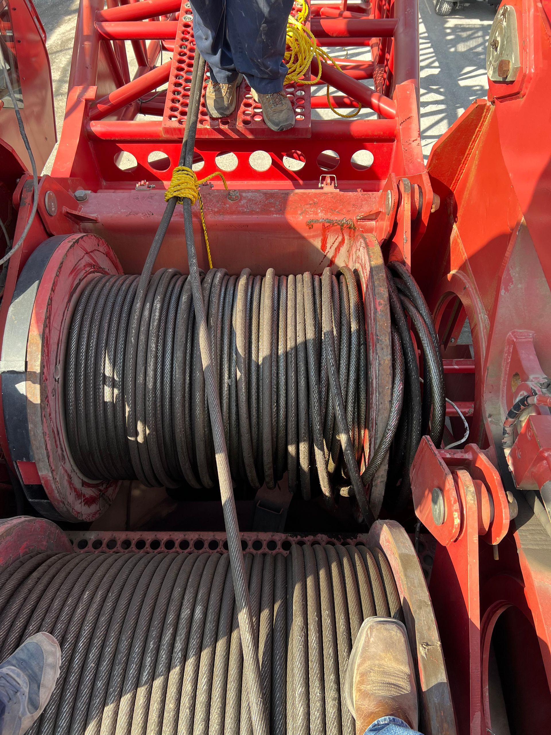 Close-up of a crane's steel cable spool with a person standing above. The cable is wound on the spool.